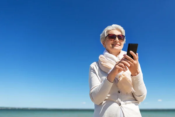 Seniorin nutzt Smartphone am Strand — Stockfoto
