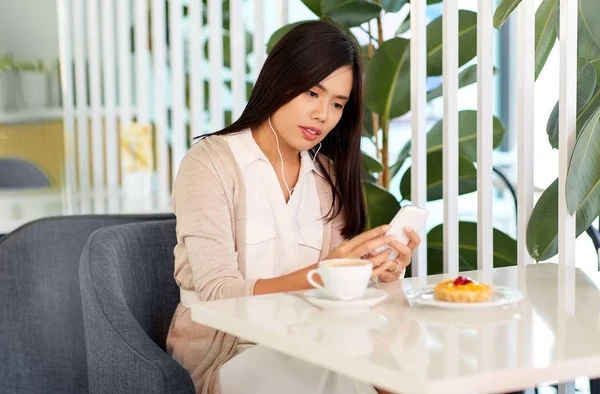 카페에서 스마트폰 과 이어폰을 가진 아시아 여성 — 스톡 사진