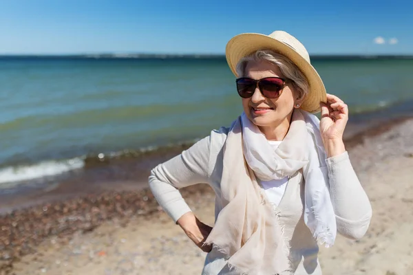 Щаслива старша жінка в сонцезахисних окулярах і капелюсі на пляжі Ліцензійні Стокові Зображення