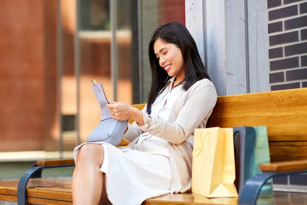 Asian woman with shopping bags on bench in city — Stock Photo, Image