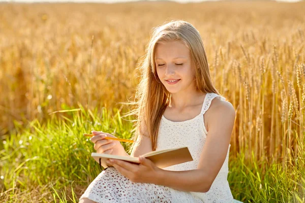 Chica sonriente escribiendo a diario en el campo de cereales — Foto de Stock