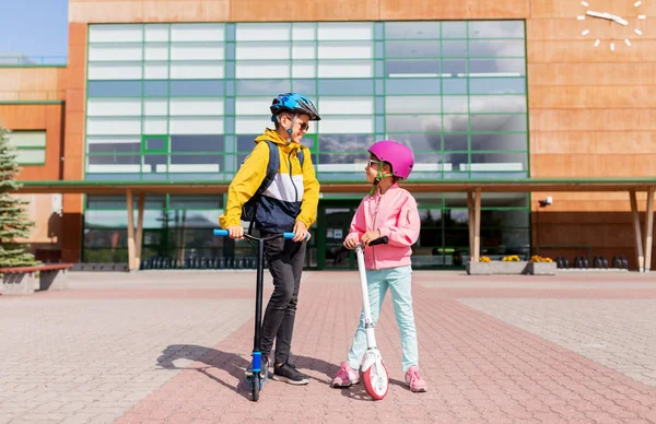 Gelukkig schoolkinderen in helmen rijden scooters — Stockfoto