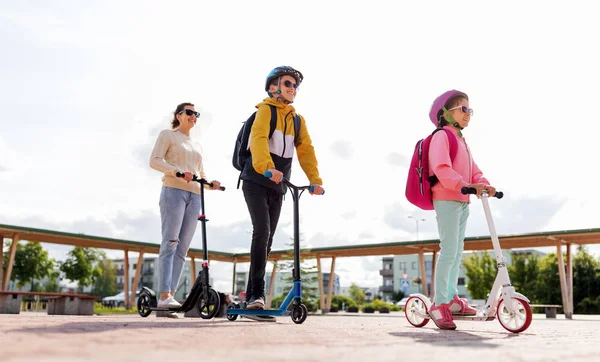 Gelukkig schoolkinderen met moeder paardrijden scooters — Stockfoto