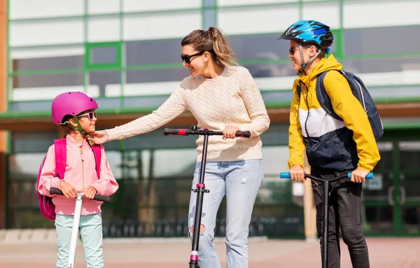 Gelukkig schoolkinderen met moeder paardrijden scooters — Stockfoto