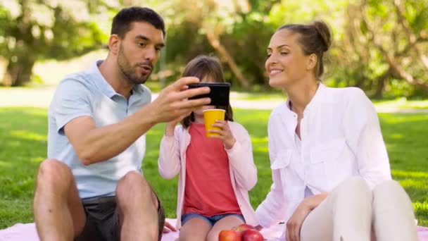Familia haciendo picnic y tomando selfie en el parque — Vídeo de stock