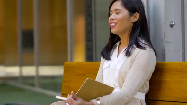 Asian woman with notebook drinking coffee on bench — Stock Video