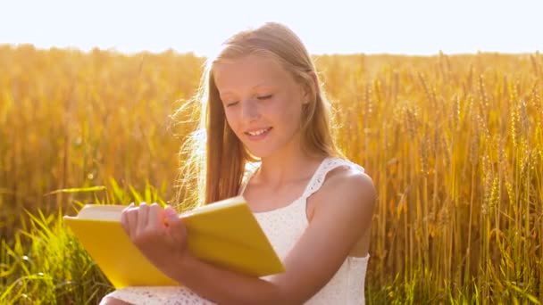 Sorridente jovem leitura livro sobre campo de cereais — Vídeo de Stock