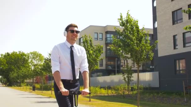 Uomo d'affari con cuffie equitazione scooter in città — Video Stock