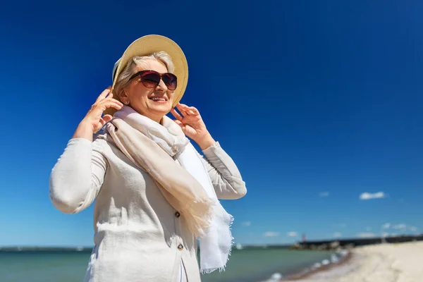 Szczęśliwa starsza kobieta w okularach przeciwsłonecznych i kapeluszu na plaży — Zdjęcie stockowe