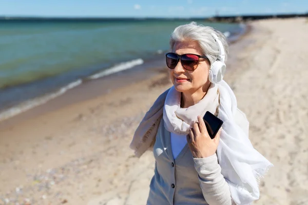 Vieille femme en casque avec smartphone sur la plage — Photo