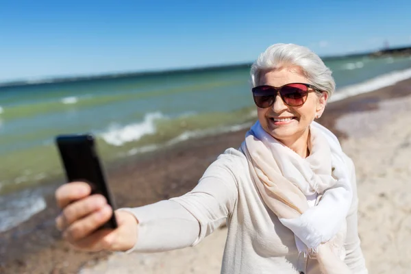 Senior vrouw neemt selfie met smartphone op het strand — Stockfoto