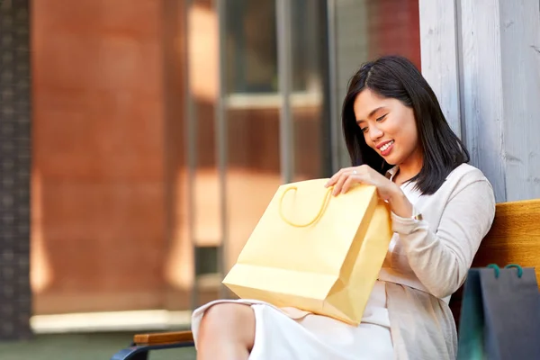 Mulher asiática com sacos de compras no banco na cidade — Fotografia de Stock