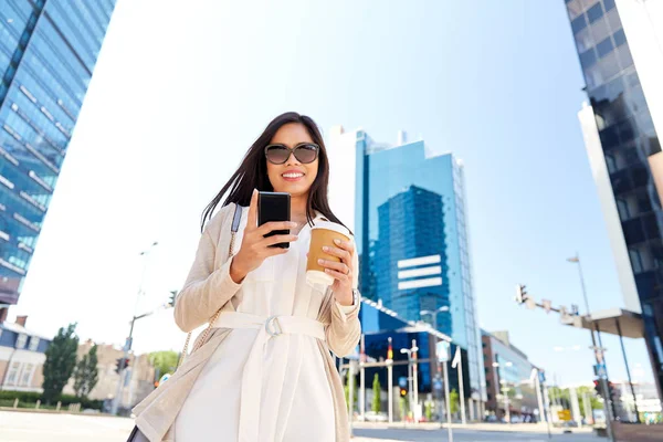 Улыбающаяся женщина со смартфоном и кофе в городе — стоковое фото