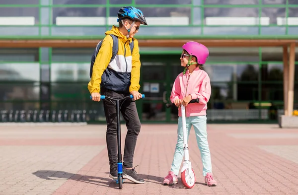 Gelukkig schoolkinderen in helmen rijden scooters — Stockfoto