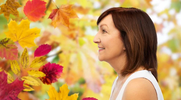 Perfil de mujer mayor sonriente sobre hojas de otoño — Foto de Stock