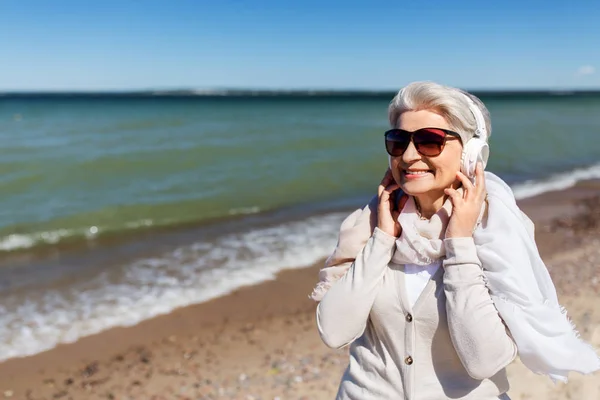 Mulher velha em fones de ouvido ouve música na praia — Fotografia de Stock