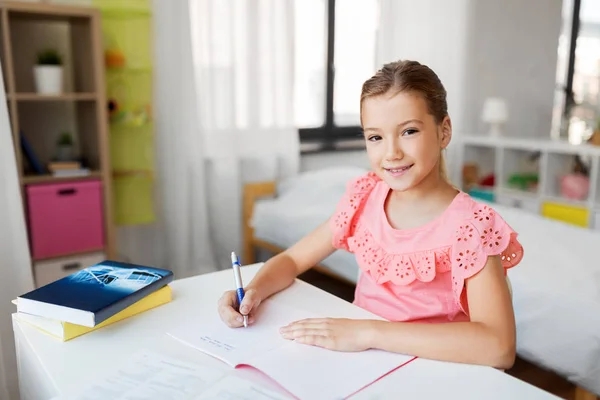 Estudante menina com livro escrevendo para notebook em casa — Fotografia de Stock