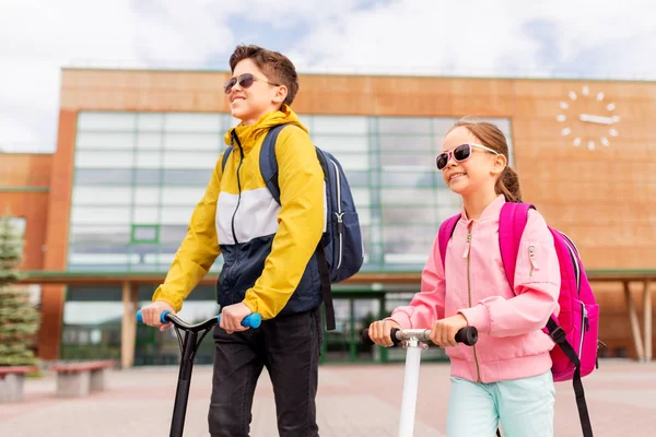 Skolbarn med ryggsäckar ridning skotrar — Stockfoto