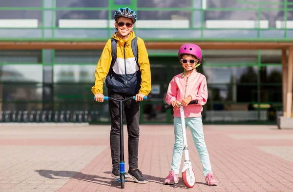 Gelukkig schoolkinderen in helmen rijden scooters — Stockfoto