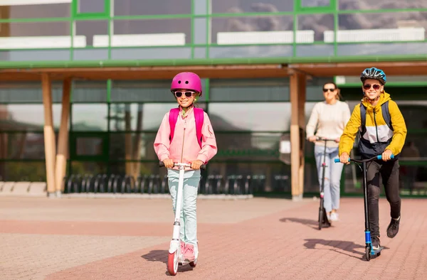 Gelukkig schoolkinderen met moeder paardrijden scooters — Stockfoto