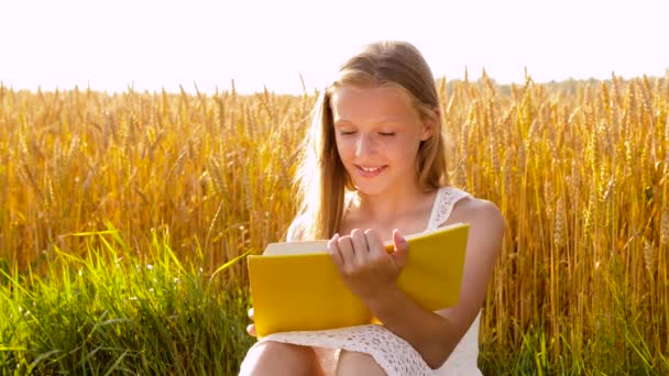 Uśmiechnięta młoda dziewczyna czytania książki na polu zbóż — Wideo stockowe