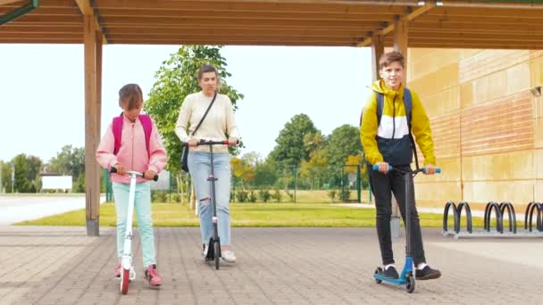 Glada skolbarn med mamma ridning skotrar — Stockvideo