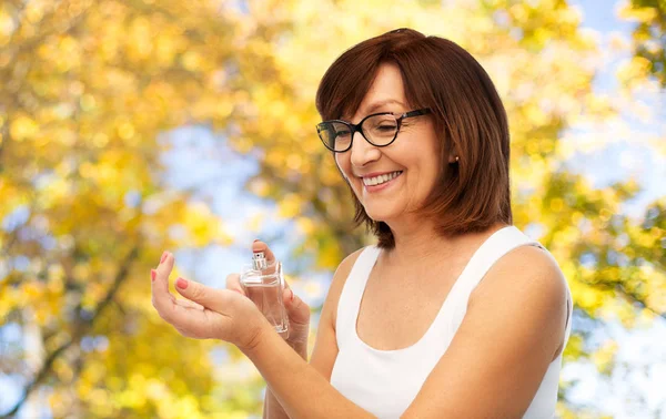 Sonriente mujer mayor rociando perfume a su muñeca —  Fotos de Stock