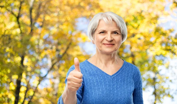 Starší žena r ukazující palce v podzimní parku — Stock fotografie