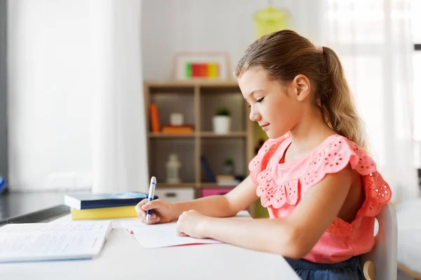 Student meisje met boek schrijven naar notebook thuis — Stockfoto