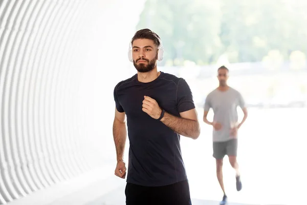 Male friends with headphones running outdoors — Stock Photo, Image