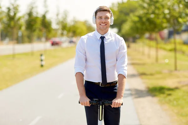 Homem de negócios com fones de ouvido montando scooter na cidade — Fotografia de Stock