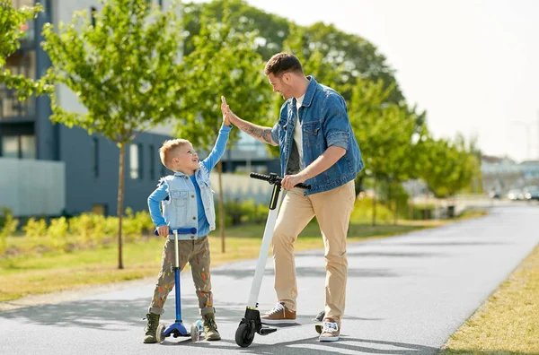 Vader en zoon met scooters maken high five — Stockfoto