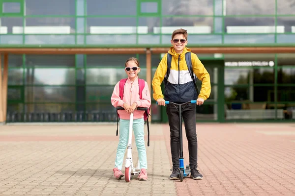 Gelukkige schoolkinderen met rugzakken en scooters — Stockfoto