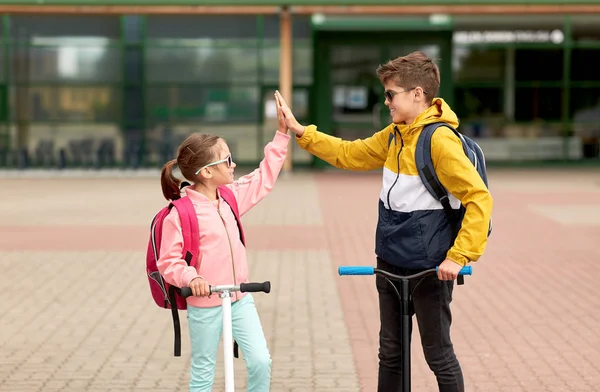 Gelukkige schoolkinderen met rugzakken en scooters — Stockfoto