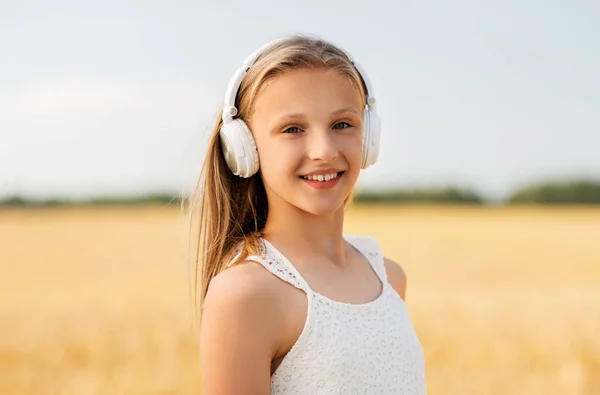 Glückliches Mädchen mit Kopfhörern auf einem Getreidefeld im Sommer — Stockfoto