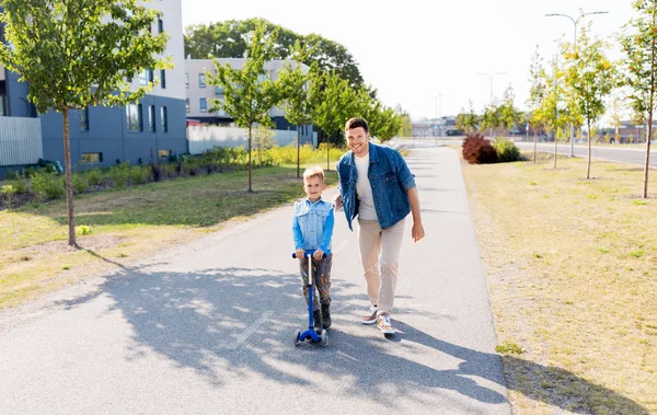 Gelukkig vader en zoontje paardrijden scooter in stad — Stockfoto