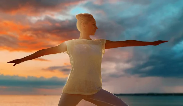 Mujer haciendo guerrero pose sobre mar puesta de sol — Foto de Stock