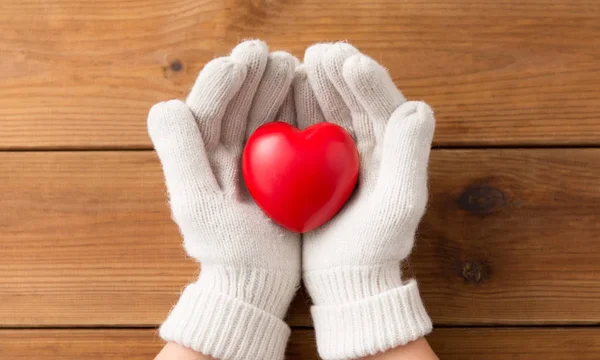 Manos en guantes de lana blanca sosteniendo el corazón rojo — Foto de Stock
