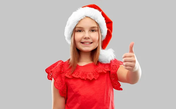 Smiling girl in snata helper hat showing thumbs up — Stock Photo, Image