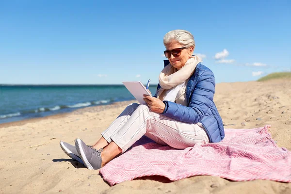 Mujer mayor escribiendo a cuaderno en la playa de verano —  Fotos de Stock