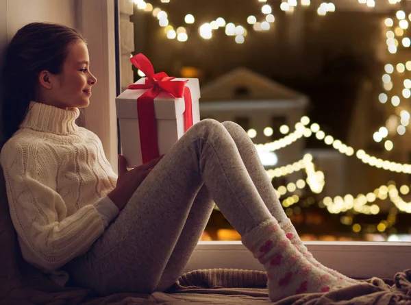 Κορίτσι με χριστουγεννιάτικο δώρο κάθεται στο περβάζι παράθυρο — Φωτογραφία Αρχείου