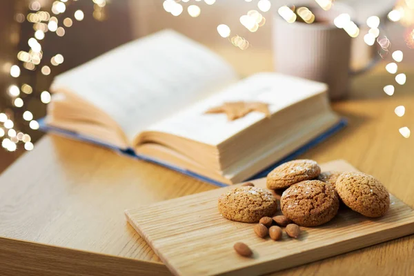 Biscoitos de aveia, amêndoas e livro na mesa em casa — Fotografia de Stock