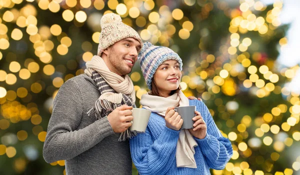 Couple heureux avec des tasses sur les lumières de Noël — Photo