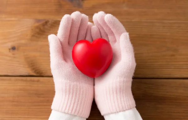 Χέρια σε ροζ μάλλινα γάντια κρατώντας κόκκινη καρδιά — Φωτογραφία Αρχείου