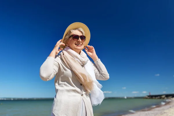 Happy senior woman in sunglasses and hat on beach — Stock Photo, Image