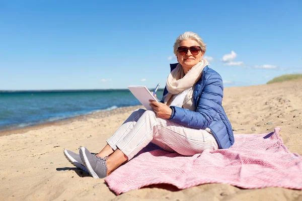 Старшая женщина пишет в блокнот на пляже — стоковое фото