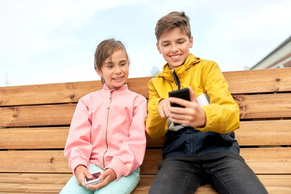 Barn med smartphones sitter på gatbänk — Stockfoto