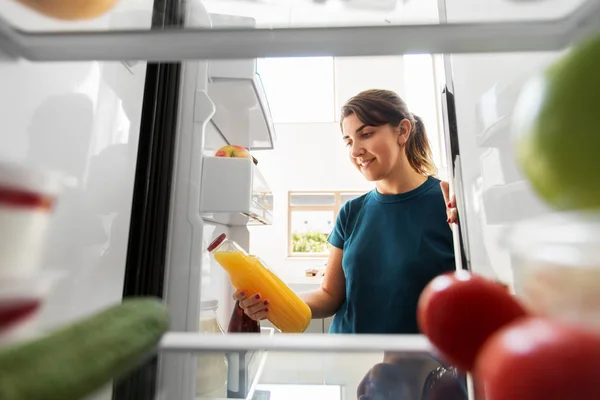 Lycklig kvinna tar saft från kylskåp hemma — Stockfoto