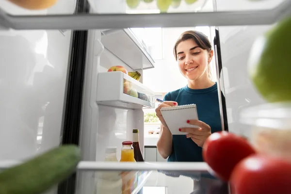 Kvinna gör lista över nödvändig mat hemma kylskåp — Stockfoto
