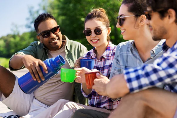 Šťastní přátelé pijící čaj z termosky v létě — Stock fotografie